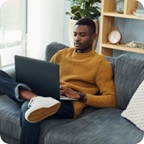 Man lounges on couch and holds laptop. 